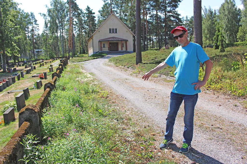 Perhosharrastaja, kanttori Jukka Tabell osoittaa muurin vieressä olevaa viherkaistaa, jossa rikkakasvien juurien poisto ja sorastaminen edesauttaisi pikkusinisiiven toukan ravintokasvien siirtoa ja kasvua. Toimenpide vähentäisi jatkossa seurakunnan hoitotyötä. Kuva: Esa Arvekari